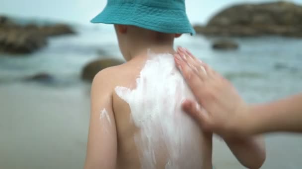 Madre aplicando crema protector solar en el hijo de vuelta en la playa
. - Imágenes, Vídeo
