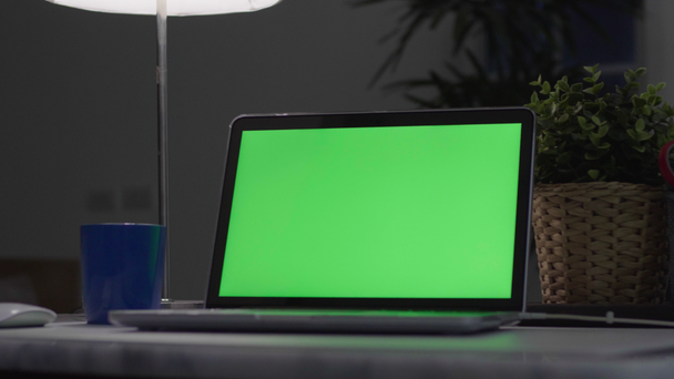 Φορητός υπολογιστής με πράσινη οθόνη. Σκοτεινό γραφείο. Πυροβολήστε την Ντόλι. Ιδανικό για να τοποθετήσετε τη δική σας εικόνα ή βίντεο. Χρησιμοποιείται πράσινη οθόνη τεχνολογίας. Φορητός υπολογιστής κλειδιών αποχρώσεων - Πλάνα, βίντεο