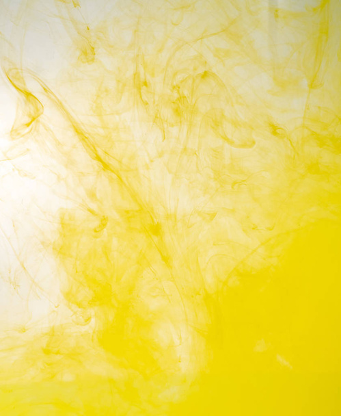 Yellow acrylic paint dissolving into water, close up view. Blurred background. Yellow abstract pattern of ink in liquid. Acrylic clouds mixing with water, abstract background. - Foto, imagen