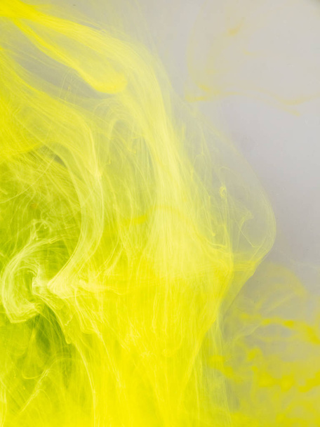 Transformation of ink droplet in water, close up view. Blurred background. Yellow paint dissolving into water, abstract pattern. Acrylic clouds in liquid, abstract background. Ink swirling in liquid. - Foto, afbeelding