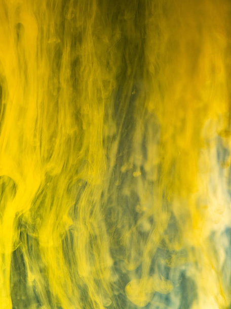 Pintura amarilla disolviéndose en agua, vista cercana. Fondo borroso. La tinta acrílica fluye mezclándose con un patrón líquido y abstracto. Gotita de transformación de tinta en agua, fondo abstracto
 - Foto, Imagen