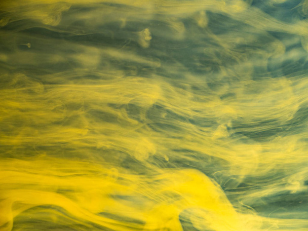 Abstract flows of yellow paint in water, close up view. Blurred background. Droplet of acrylic ink dissolving into water, abstract pattern. Ink mixing with liquid, abstract background. - Foto, imagen