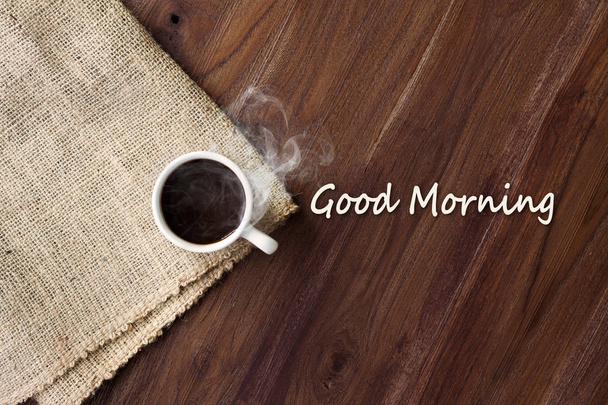 Cup of hot coffee with smoke on wooden table top view with word good morning. coffee background with copy space - Фото, изображение