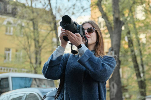 Beautiful young woman with camera in city. Tourist girl traveling and photographing, spring city street background - Fotografie, Obrázek