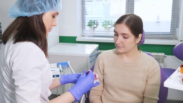 Γυναίκα οδοντίατρος δείχνει στον ασθενή σε ένα μοντέλο σαγόνι πώς να καθαρίσετε τα δόντια με οδοντόβουρτσα σωστά. - Πλάνα, βίντεο