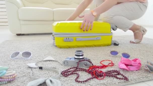 Travel and vacation concept. Happy young woman is packing colorful summer clothes into luggage suitcase for a new journey - 映像、動画