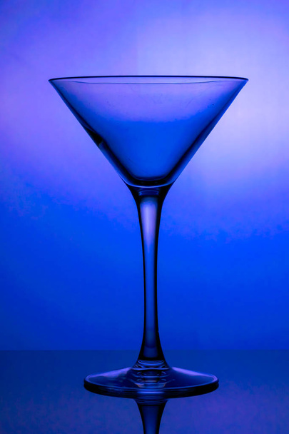 Cocktailglas, das gestielte Glas wird mit blauem Licht beleuchtet - Foto, Bild