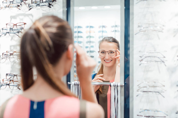 Jovem mulher tentando óculos de moda na loja optometrista - Foto, Imagem