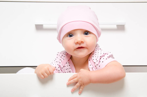 Portrait of a cute happy baby sitting in a drawer chest - 写真・画像