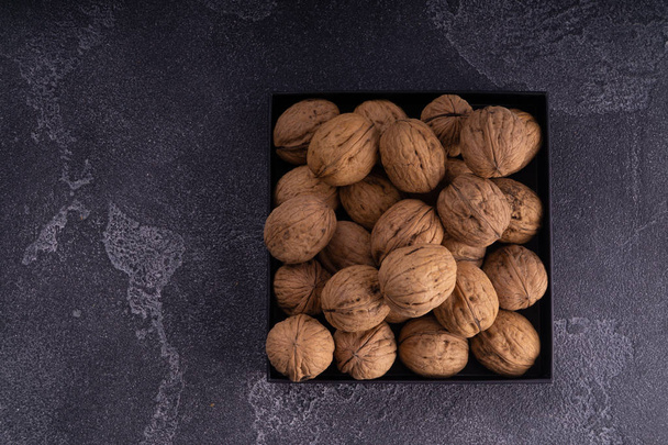 Whole and cracked walnuts on a square plate on blue textured surface, top view. Healthy nuts and seeds composition. - Foto, Imagem