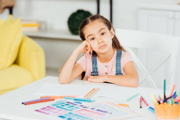 selective focus of upset kid looking at camera near papers with drawing  - Foto, Imagen
