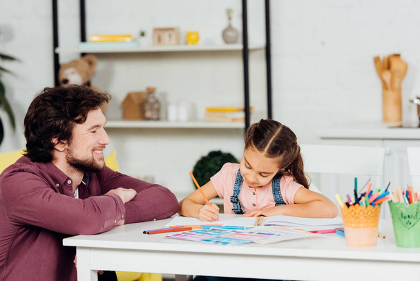 happy father looking at cute daughter drawing at home  - Photo, Image