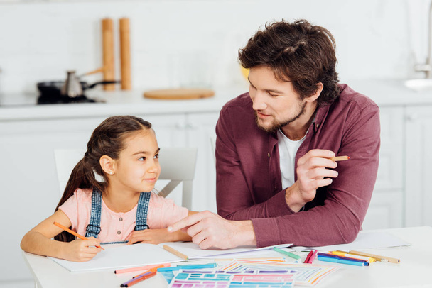 cute daughter looking at handsome father pointing with finger at paper  - Фото, зображення