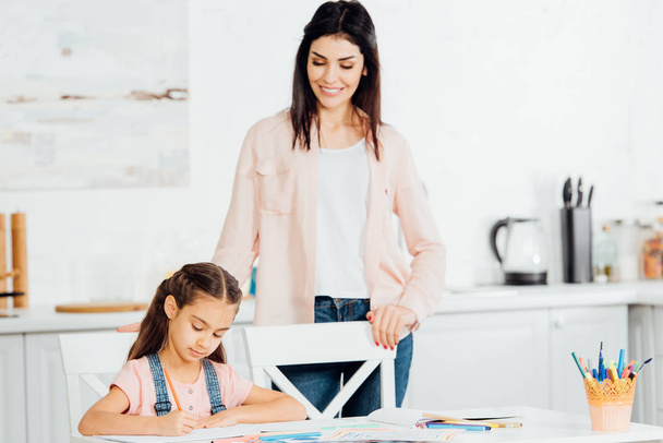 attractive mother looking at cute daughter drawing at home  - Φωτογραφία, εικόνα