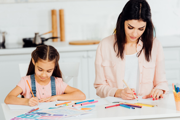 attractive brunette mother and cute daughter drawing at home  - Фото, изображение