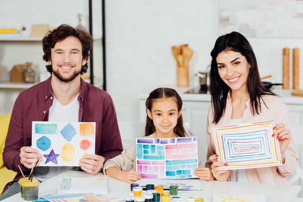 cheerful kid and happy father and mother holding papers with drawing at home  - Photo, Image