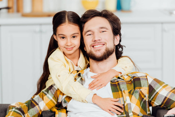 happy daughter hugging cheerful bearded father at home  - Фото, изображение
