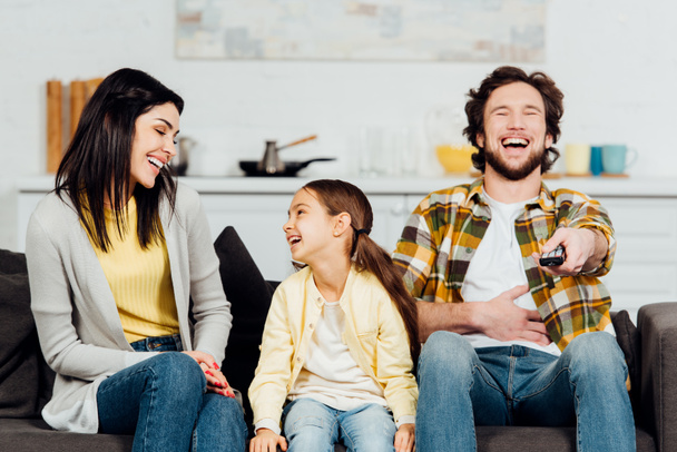 happy father laughing while watching tv near attractive wife and kid  - Fotoğraf, Görsel