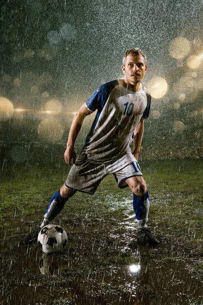 Soccer player on professional soccer night rain stadium. Dirty player in rain drops with football ball - Photo, Image