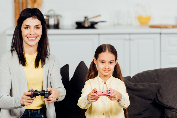 happy kid playing with cheerful mother holding joystick at home  - Фото, изображение