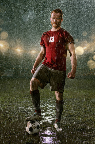 Jogador de futebol no estádio de futebol profissional noite chuva. Jogador sujo na chuva cai com bola de futebol
 - Foto, Imagem