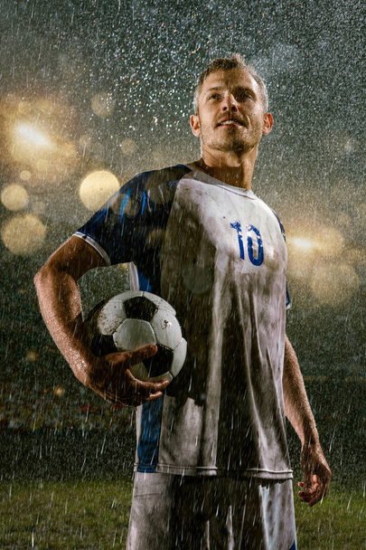 Soccer player on professional soccer night rain stadium. Dirty player in rain drops with football ball - Photo, Image