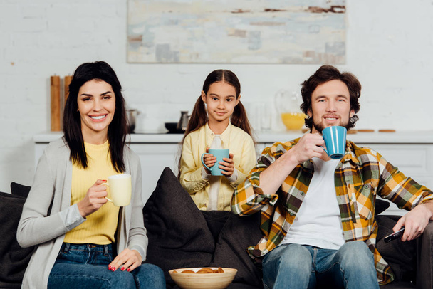 happy family holding cups with drinks near bowl with tasty cookies  - Zdjęcie, obraz