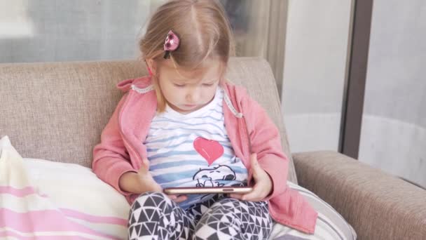 Beautiful little girl is watching a cartoon in a mobile phone - Materiał filmowy, wideo