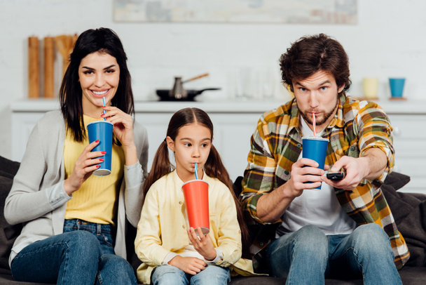 man and adorable daughter drinking soda near happy wife at home  - Foto, Imagen