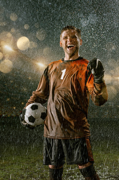 Foci kapus a profi foci éjszakai eső stadionban. Piszkos játékos eső esik futball-labda - Fotó, kép