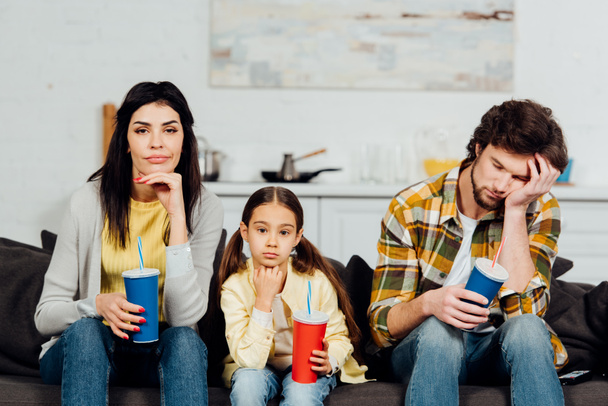 znudzony rodzina trzyma jednorazowe kubki podczas oglądania filmu w domu  - Zdjęcie, obraz
