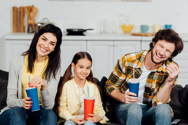 happy family holding plastic cups while watching movie at home  - Photo, Image