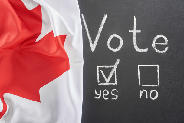 vista superior de las letras de voto y marca de verificación cerca de sí palabra en pizarra negra cerca de la bandera canadiense - Foto, Imagen