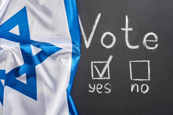 vista superior de la palabra de voto y marca de verificación cerca de sí palabra en pizarra negra cerca de la bandera de Israel
 - Foto, Imagen