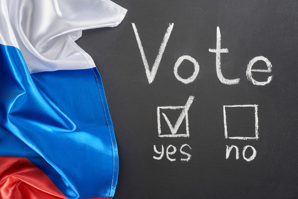 top view of vote lettering and check mark near yes word on black chalkboard near flag of Russia - Фото, зображення