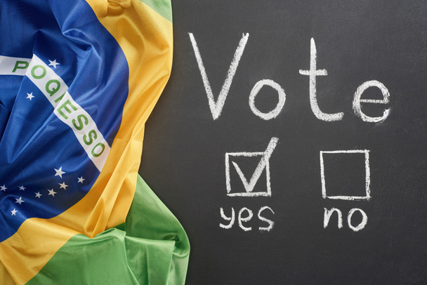 vista superior de letras de voto branco e marca de verificação perto sim palavra no quadro preto perto da bandeira do Brasil
 - Foto, Imagem