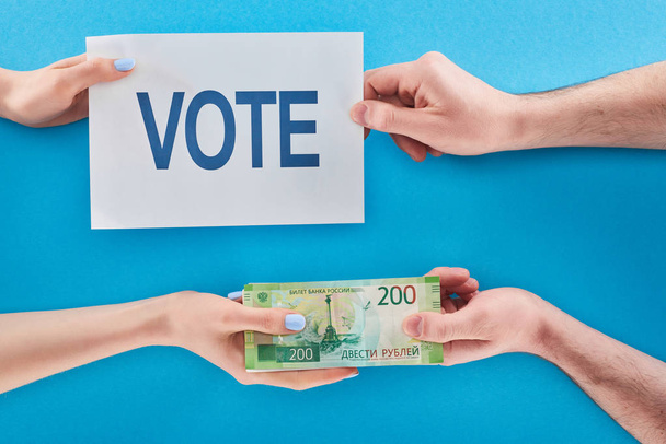 Teilansicht der Frau, die dem Mann auf blauem Hintergrund Bestechungsgeld für die Stimmabgabe in Rubel gibt - Foto, Bild