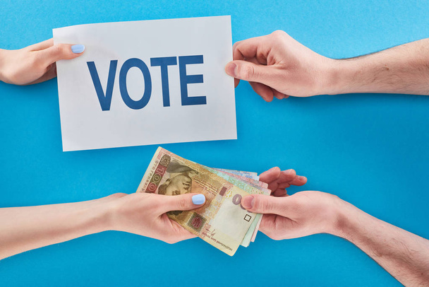partial view of woman giving ukrainian hryvni for vote to man on blue background - Photo, Image