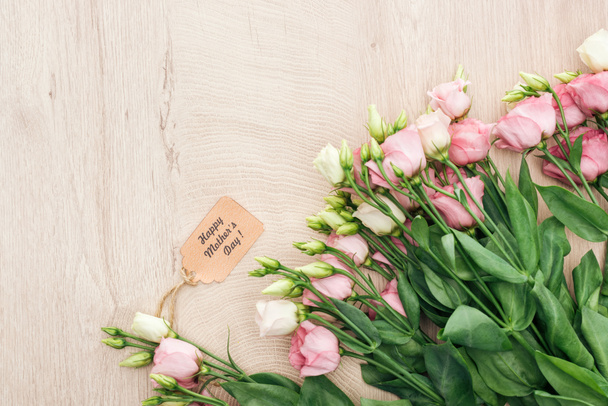 top view of eustoma flowers with happy mothers day paper label on wooden table with copy space - Fotografie, Obrázek