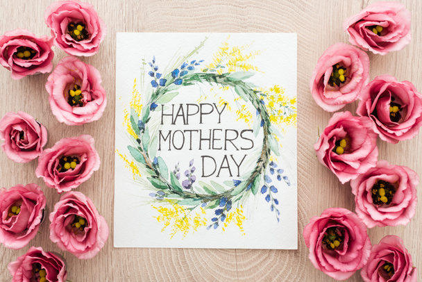 vista dall'alto di fiori di eustoma e carta con felice giorno delle madri scrivendo sulla superficie di legno
 - Foto, immagini