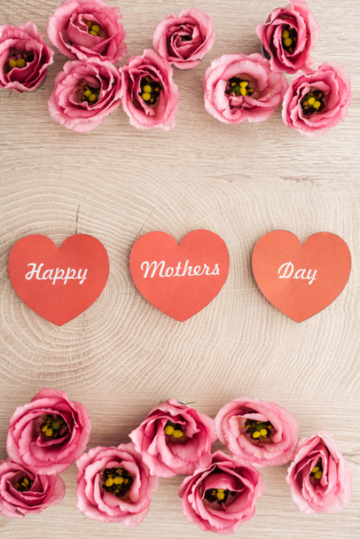 Κορυφαία θέα των καρτών σε σχήμα καρδιάς με ευτυχισμένη ημέρα της μητέρας γραφής και ευστόμα λουλούδια σε ξύλινο τραπέζι - Φωτογραφία, εικόνα