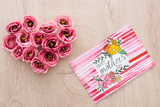 Herzschild aus Eustoma-Blumen und Karte mit Happy Mother Day Schriftzug auf Holzoberfläche - Foto, Bild