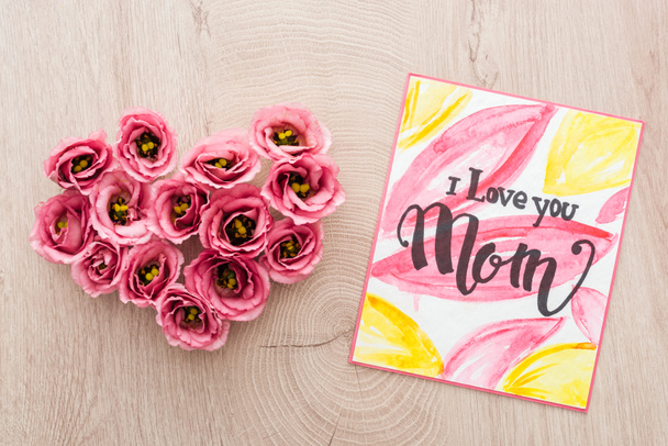 top view of heart sign made of eustoma flowers and card with i love you mom lettering on wooden table - Photo, Image