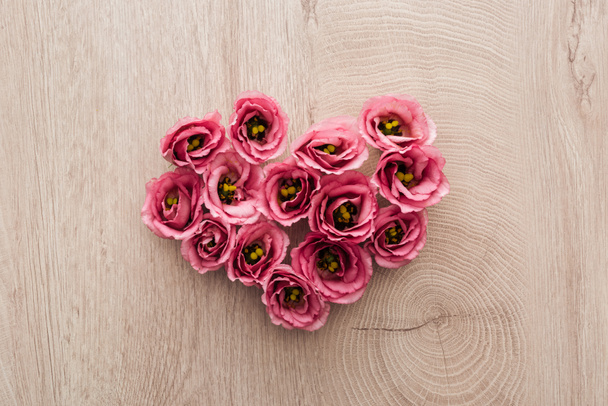 Top weergave van hart teken gemaakt van roze Eustoma bloemen op houten tafel - Foto, afbeelding