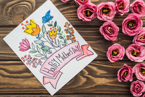 vista superior de flores de eustoma y tarjeta con felicitación feliz día de las madres en la mesa de madera
 - Foto, imagen
