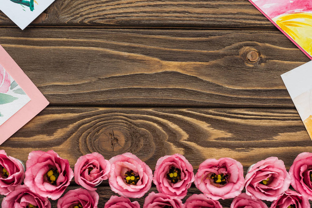 Draufsicht auf rosa Eustoma-Blumen und Zeichnungen auf Holztisch mit Kopierraum - Foto, Bild