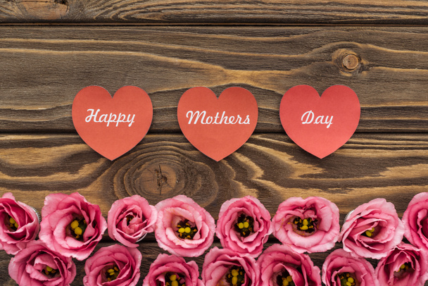 сверху вид розовых цветов эустомы и красных бумажных сердец с надписью "День матери" на деревянном столе
 - Фото, изображение
