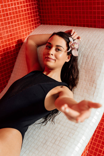 attraente giovane donna in costume da bagno sdraiata con mano tesa nel centro benessere
 - Foto, immagini