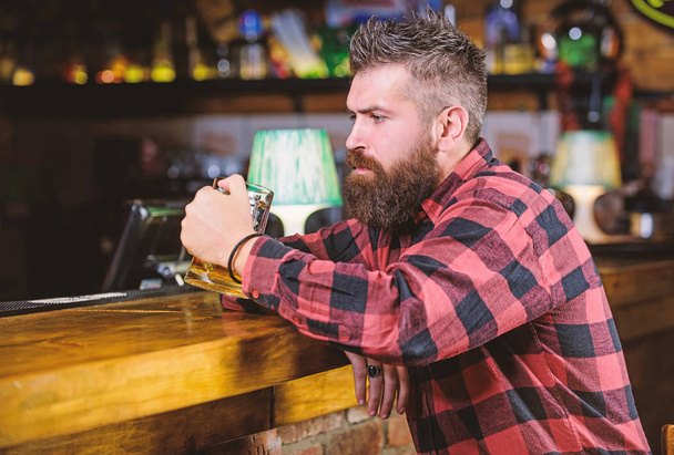 Man with beard spend leisure in dark bar. Hipster relaxing at bar with beer. Brutal hipster bearded man sit at bar counter drink beer. Order alcohol drink. Bar is relaxing place have drink and relax - Foto, Imagen