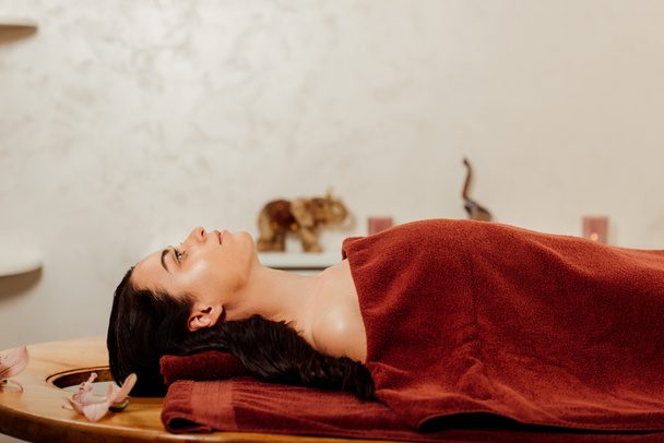 боковой вид женщины, лежащей под полотенцем на массажном столе
 - Фото, изображение